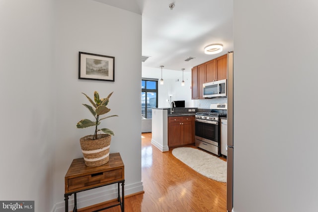 kitchen featuring appliances with stainless steel finishes, decorative backsplash, pendant lighting, light wood-type flooring, and kitchen peninsula