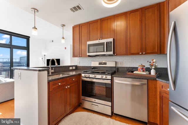 kitchen featuring dark stone countertops, sink, appliances with stainless steel finishes, decorative backsplash, and pendant lighting