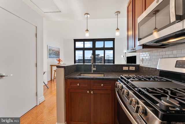 kitchen with light hardwood / wood-style flooring, tasteful backsplash, hanging light fixtures, stainless steel appliances, and sink