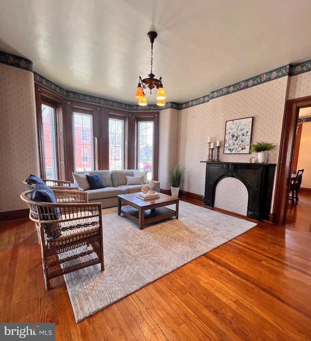 living area with a fireplace, wallpapered walls, baseboards, and wood finished floors