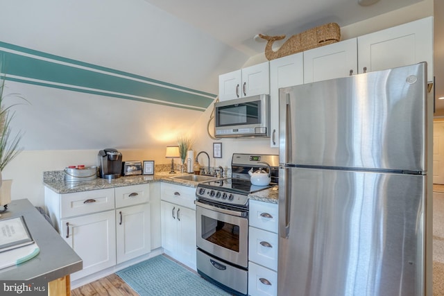 kitchen featuring lofted ceiling, sink, stainless steel appliances, light stone counters, and white cabinets