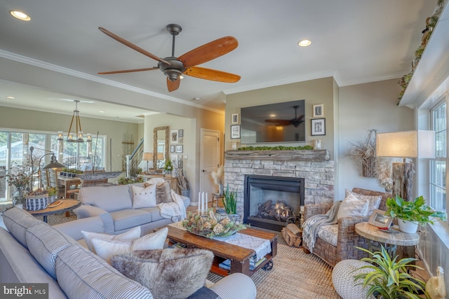 living room featuring ornamental molding, a healthy amount of sunlight, a stone fireplace, and ceiling fan with notable chandelier