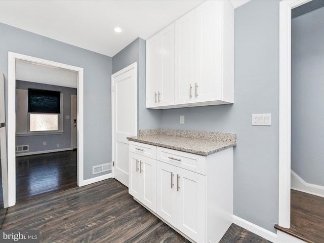 kitchen with dark wood-type flooring, light stone counters, and white cabinets