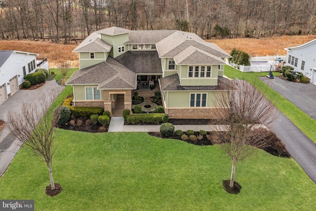 view of front of property with a shingled roof, stone siding, and a front lawn