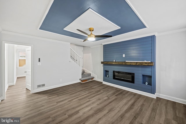 unfurnished living room with dark hardwood / wood-style floors, a large fireplace, ceiling fan, a tray ceiling, and crown molding