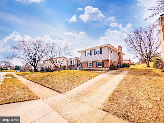 view of front of home featuring a front yard, brick siding, and a chimney