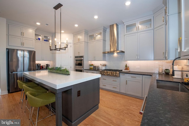 kitchen with a kitchen island, decorative light fixtures, sink, stainless steel appliances, and wall chimney exhaust hood