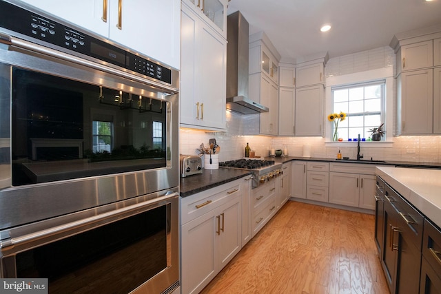 kitchen featuring appliances with stainless steel finishes, tasteful backsplash, white cabinetry, sink, and wall chimney range hood