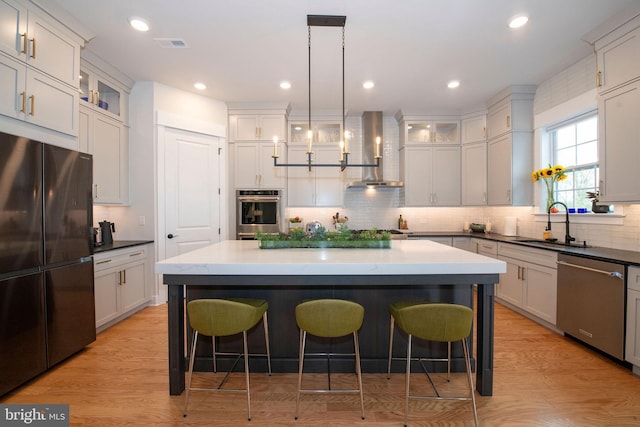 kitchen featuring pendant lighting, stainless steel appliances, a center island, and wall chimney exhaust hood