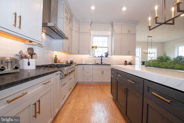 kitchen with hanging light fixtures, white cabinets, stainless steel gas stovetop, and wall chimney exhaust hood