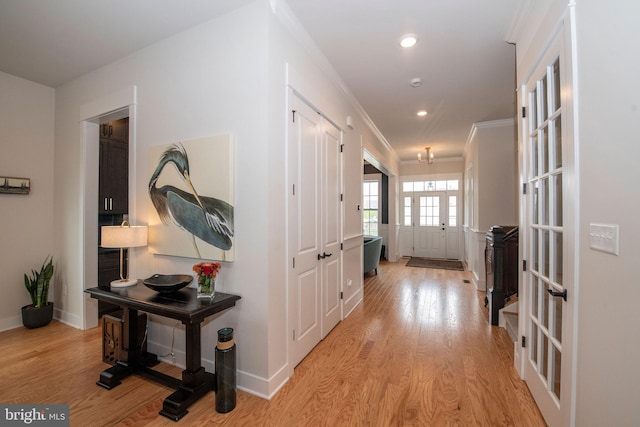 hallway with ornamental molding, light wood-type flooring, and french doors