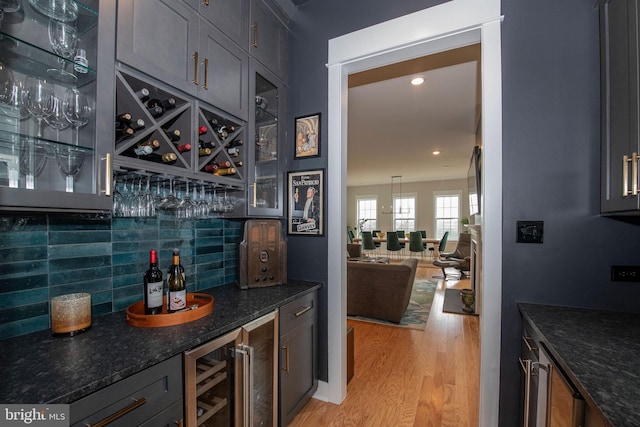 bar featuring wine cooler, dark stone counters, light hardwood / wood-style floors, and tasteful backsplash