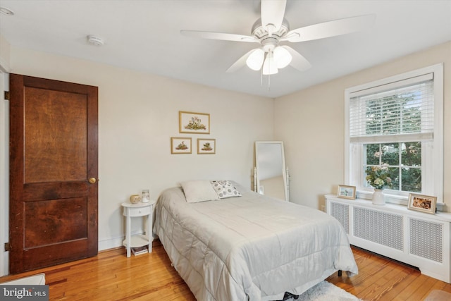 bedroom with ceiling fan, radiator heating unit, and light wood-type flooring