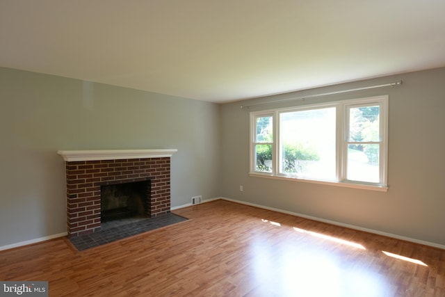 unfurnished living room featuring visible vents, a fireplace, baseboards, and wood finished floors