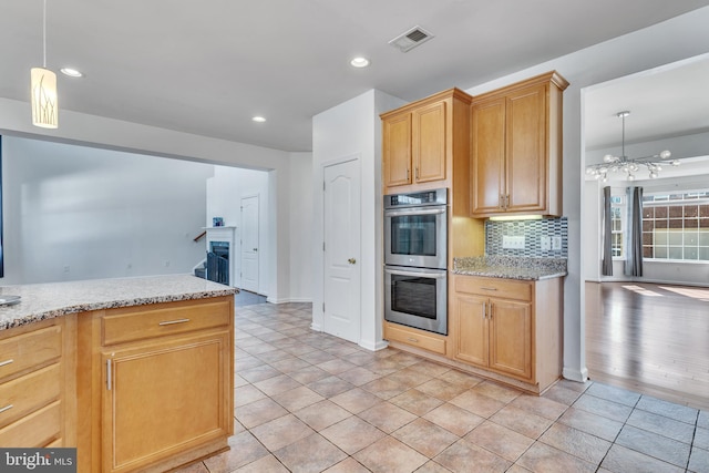 kitchen with light tile patterned floors, a chandelier, stainless steel double oven, backsplash, and light stone countertops