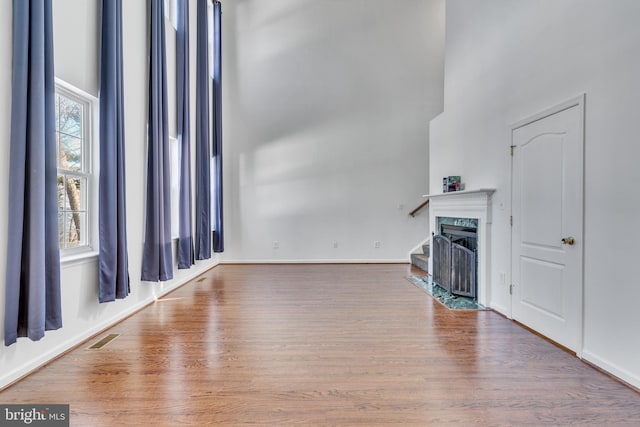 unfurnished living room with a high ceiling, visible vents, wood finished floors, and a premium fireplace