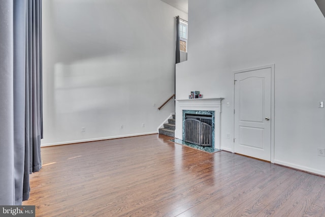 living room featuring a premium fireplace, wood finished floors, a towering ceiling, baseboards, and stairway