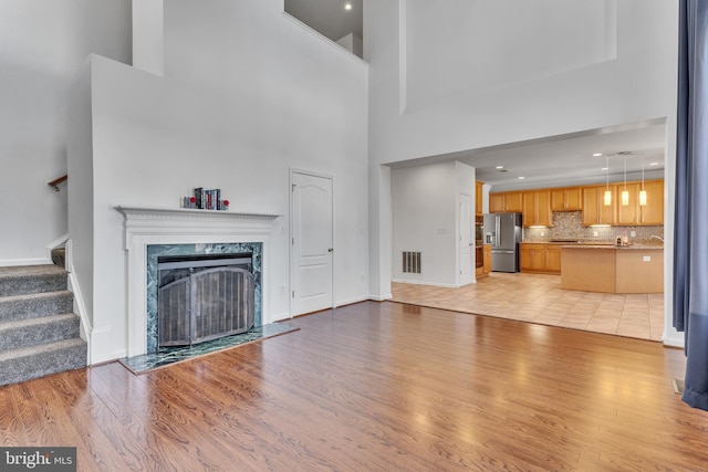 unfurnished living room featuring baseboards, visible vents, stairs, light wood-style floors, and a high end fireplace