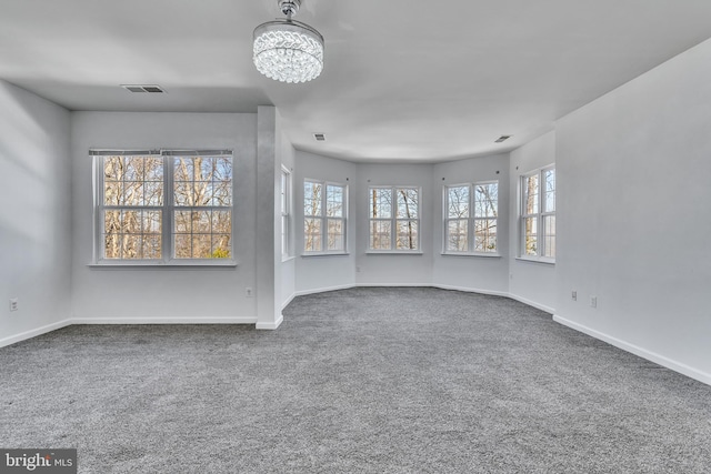 carpeted empty room with visible vents, plenty of natural light, a notable chandelier, and baseboards