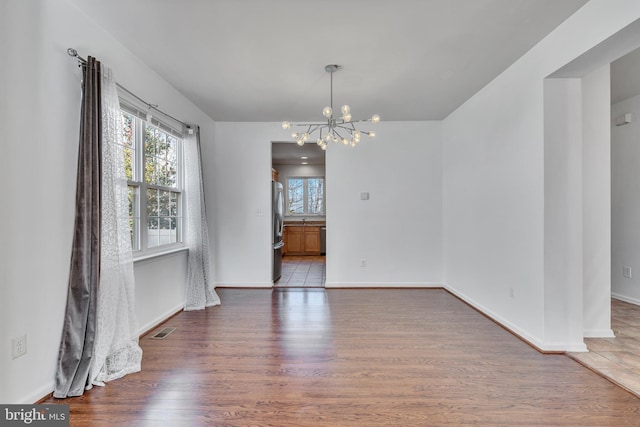 unfurnished dining area featuring baseboards, visible vents, a notable chandelier, and wood finished floors