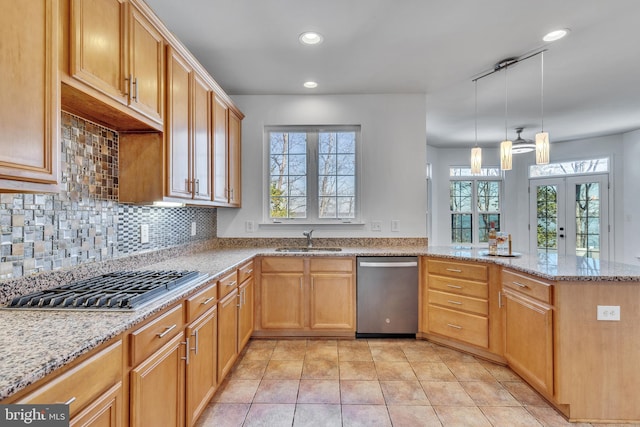 kitchen with a peninsula, a sink, appliances with stainless steel finishes, light stone countertops, and tasteful backsplash