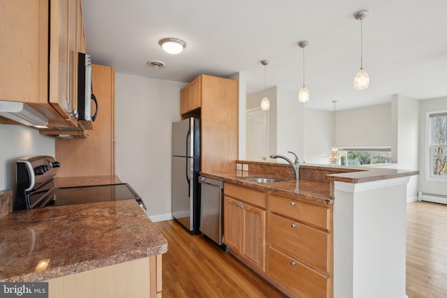 kitchen featuring appliances with stainless steel finishes, a sink, dark stone countertops, light wood finished floors, and a peninsula