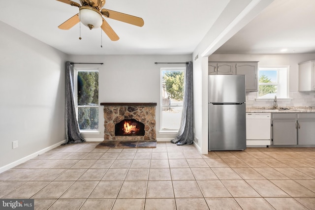 unfurnished living room with light tile patterned floors, a fireplace, sink, and ceiling fan