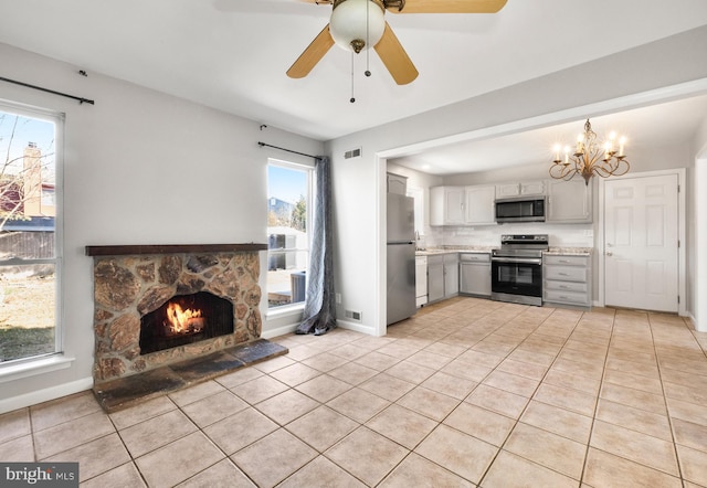 kitchen with tasteful backsplash, light tile patterned floors, appliances with stainless steel finishes, a fireplace, and ceiling fan with notable chandelier