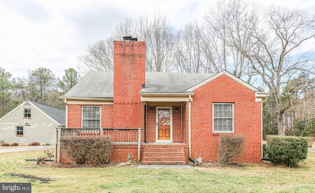 view of front facade featuring brick siding, a chimney, and a front lawn