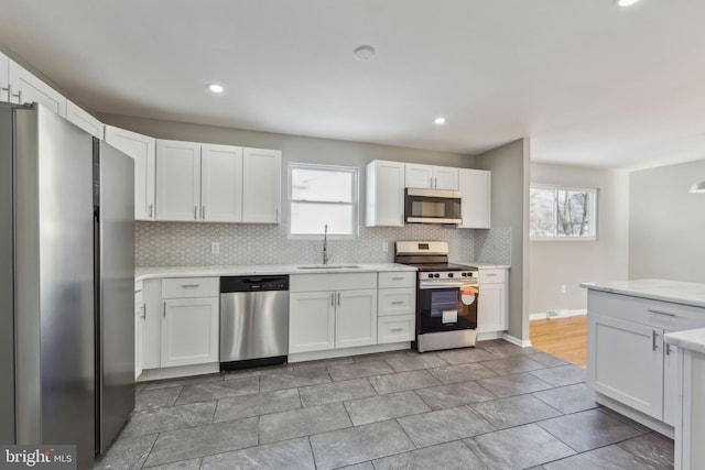 kitchen with sink, light stone counters, white cabinets, stainless steel appliances, and backsplash