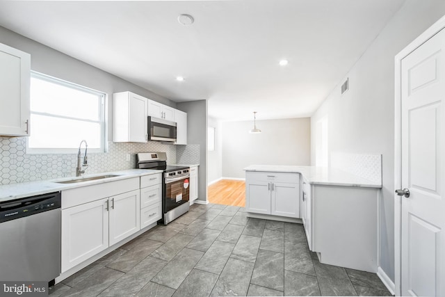 kitchen with white cabinetry, stainless steel appliances, sink, and hanging light fixtures