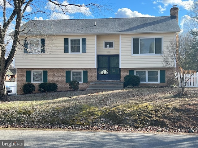 bi-level home with brick siding, a chimney, a shingled roof, and fence