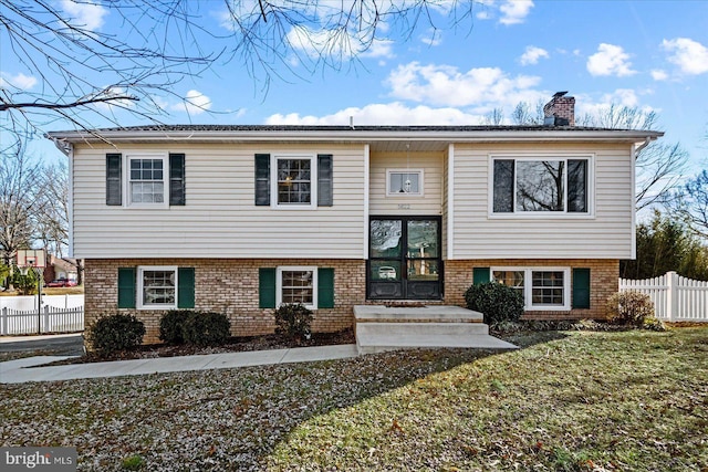 bi-level home with a front yard, a chimney, fence, and brick siding