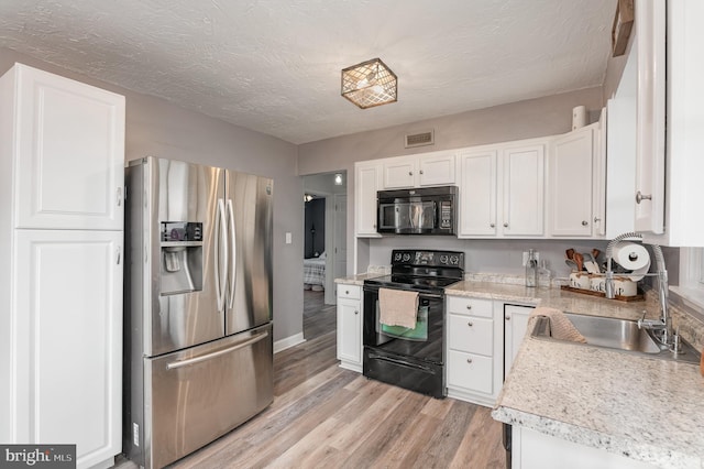 kitchen featuring white cabinetry, sink, light wood-type flooring, black appliances, and a textured ceiling