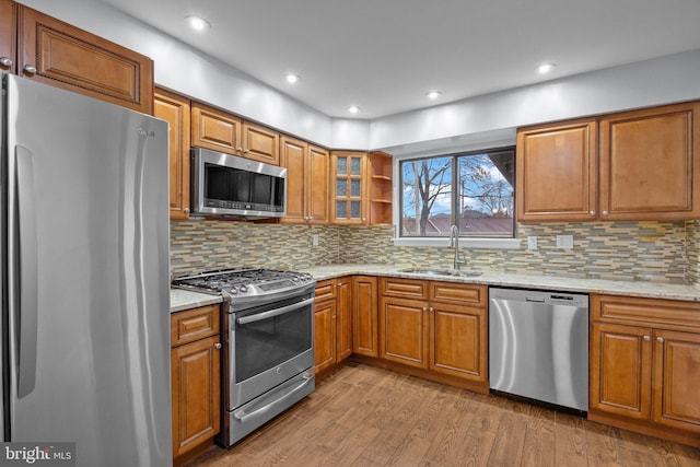 kitchen with sink, stainless steel appliances, light hardwood / wood-style floors, and light stone countertops