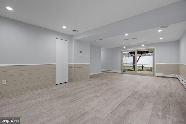 interior space featuring wood walls, baseboard heating, and light hardwood / wood-style flooring