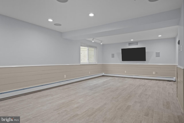 unfurnished living room with a baseboard heating unit, wooden walls, and light hardwood / wood-style floors