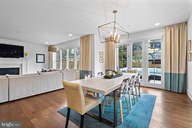 dining room with a notable chandelier, a glass covered fireplace, wood finished floors, and recessed lighting