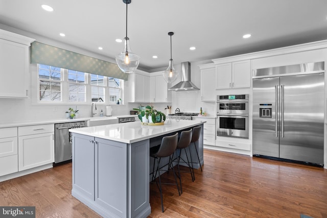 kitchen featuring appliances with stainless steel finishes, a kitchen island, wall chimney range hood, and white cabinets