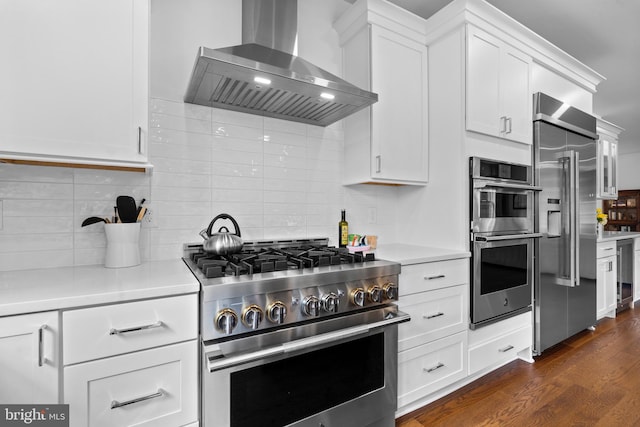 kitchen featuring high end appliances, dark wood-style flooring, light countertops, and wall chimney exhaust hood