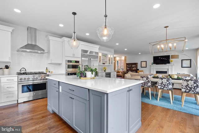 kitchen with premium appliances, light wood-style flooring, gray cabinetry, white cabinetry, and wall chimney exhaust hood