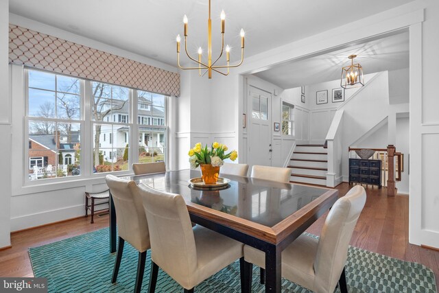 dining space with an inviting chandelier, stairway, a decorative wall, and wood finished floors