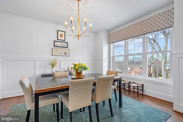 dining area with a chandelier, wainscoting, wood finished floors, and a decorative wall