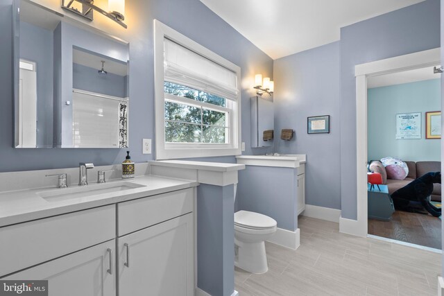 bathroom featuring baseboards, a shower with shower curtain, toilet, a sink, and two vanities