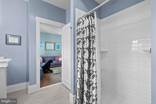 bathroom featuring wood tiled floor, baseboards, a tile shower, and connected bathroom