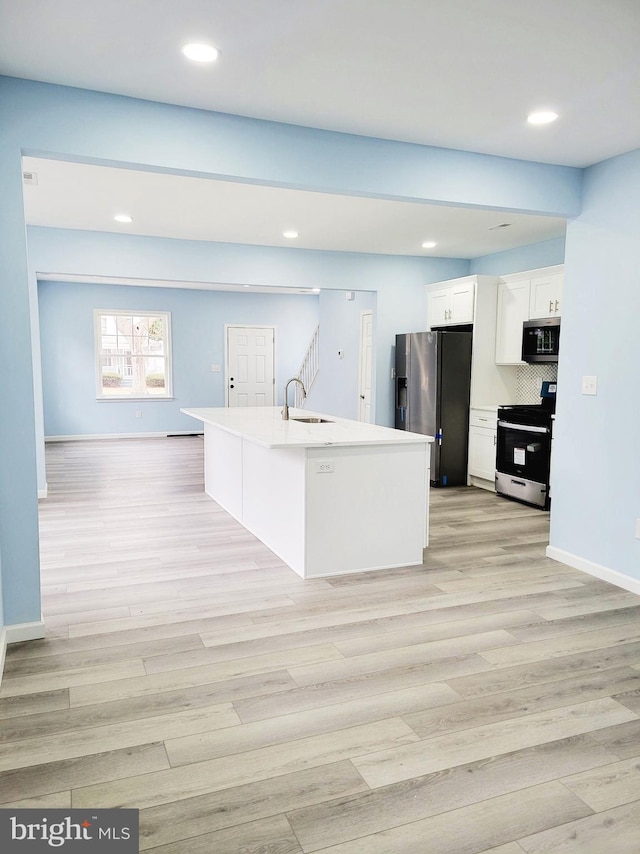 kitchen featuring white cabinetry, a center island with sink, light wood-type flooring, sink, and appliances with stainless steel finishes