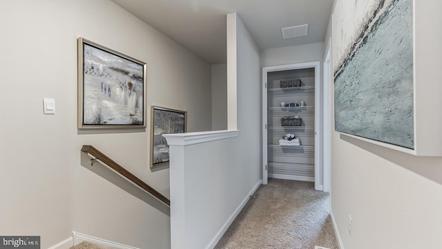 hallway featuring baseboards, visible vents, light colored carpet, and an upstairs landing