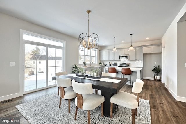 dining space with dark wood-type flooring, visible vents, a notable chandelier, and baseboards