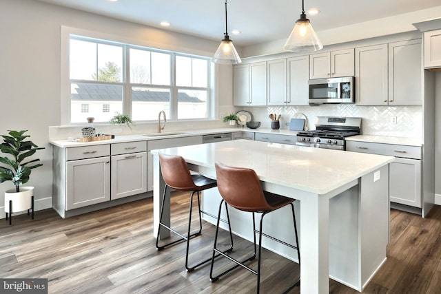 kitchen with a center island, hanging light fixtures, a sink, stainless steel appliances, and backsplash