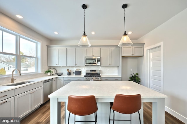 kitchen with stainless steel appliances, a sink, light countertops, a center island, and pendant lighting